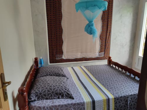 Chambre à la Résidence Les 2 Moulins au Moule : lit en bois, parure de lit à motifs et moustiquaire turquoise