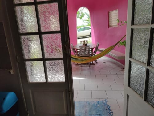 Chambre tropical rose à la Résidence Les 2 Moulins avec portes ouvertes sur balcon, hamac et vue mer en Guadeloupe