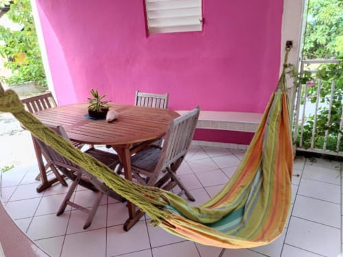 Hamac coloré et table de salle à manger en bois sur terrasse rose vif aux Résidence Les 2 Moulins, Guadeloupe