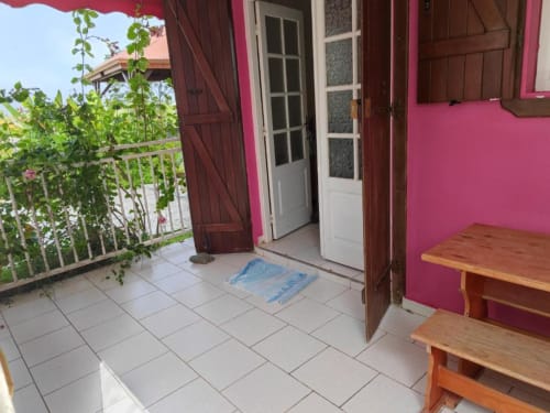 Balcon rose vif à la Résidence Les 2 Moulins au Moule avec carrelage, mobilier en bois et vue sur le jardin