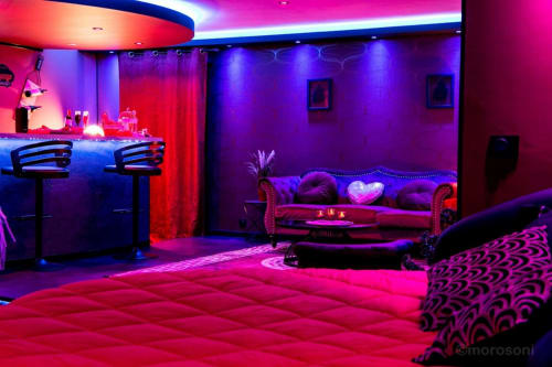 Appartement spa néon vibrant à L'Insolite à Toulouse avec sièges roses, bar et ambiance lumineuse violette