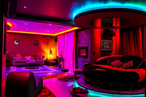 Appartement de luxe illuminé aux néons à L'Insolite Spa Privatif à Toulouse, murs magenta, lit rouge incurvé et plafond aux accents cyan