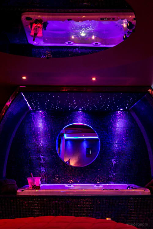 Suite spa luxueuse à L'Insolite avec plafond néon, miroir rond et éclairage ambiant violet à Toulouse