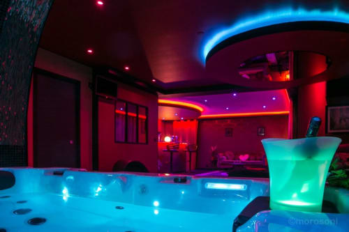 Appartement spa moderne à L'Insolite à Toulouse avec bar piscine néon, cocktail luminescent vert et ambiance vibrante rouge