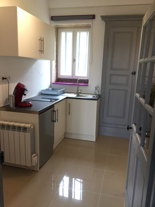 Cuisine moderne de l'appartement La Ferme du Bonheur avec armoires crème, plans de travail noirs, évier, fenêtre et sol carrelé