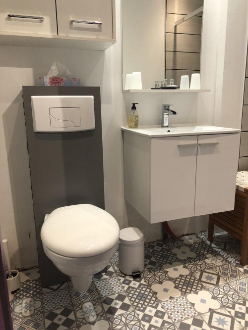 Salle de bains moderne à La Ferme du Bonheur avec vasque blanche, toilettes, carrelage à motifs et étagères murales