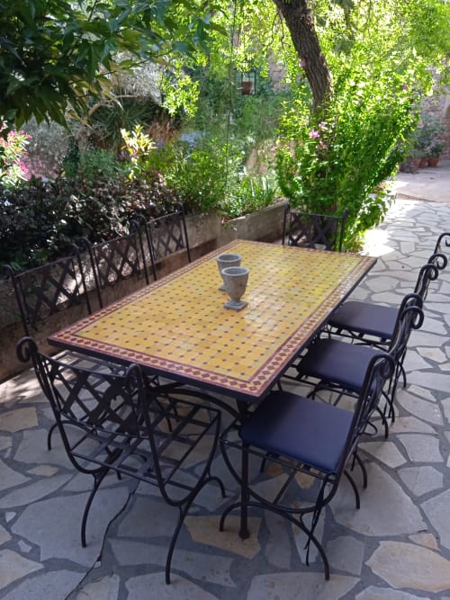 Moroccan-style dining table with yellow tile top and wrought iron chairs in lush courtyard garden at Mas des Artistes,