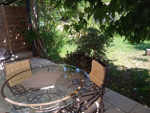 Shaded patio with round glass table and cushioned chairs overlooking lush garden at Mas des Artistes, Mouriès