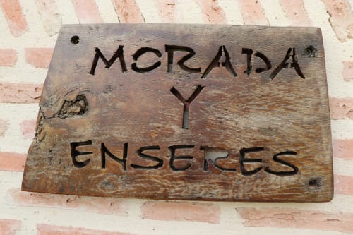 Cartel de madera con el texto 'Merada y Enserges' montado en pared de ladrillo en Apartamentos Casa Lafuente, Lukiano, Araba