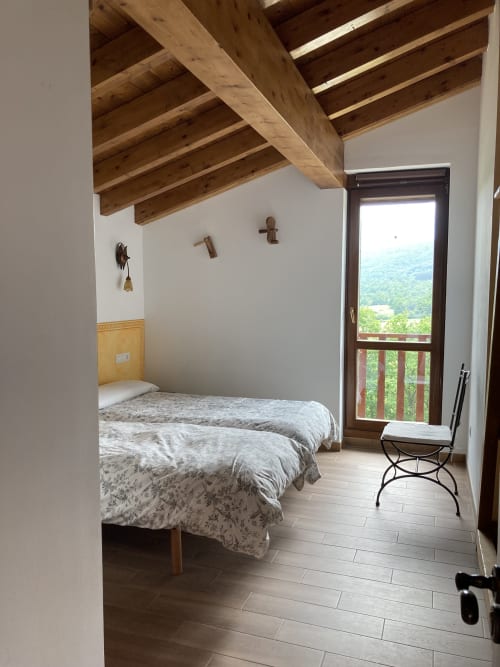 Dormitorio luminoso en Casa Lafuente con vigas de madera vista, vistas a las montañas desde la puerta del balcón y mobiliario moderno