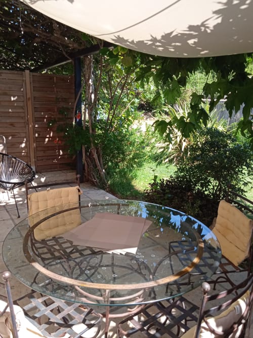 Shaded garden patio at Mas des Artistes with round glass table, cushioned chairs, and lush greenery in Mouriès