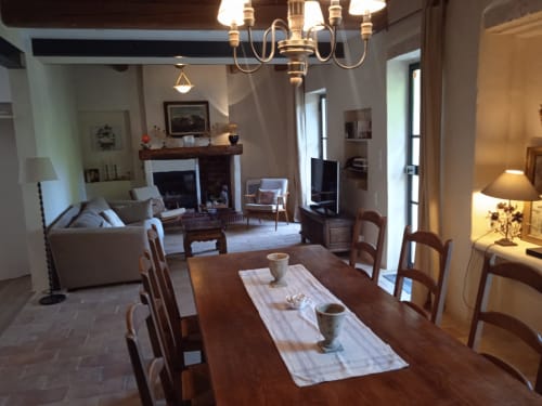 Dining area in Mas des Artistes cottage with wooden table, fireplace, and living room beyond in Mouriès