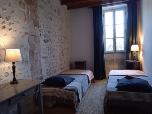 Twin bedroom in Mas des Artistes cottage, Mouriès, with stone walls, twin beds, desk lamp, and garden view window
