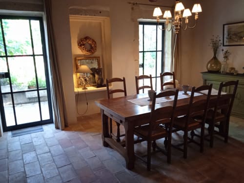 Elegant dining area in Mas des Artistes cottage with wooden table, rustic chairs, chandelier, and garden views through French