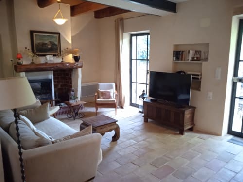 Spacious living room with fireplace, TV, cream seating, and garden views at Mas des Artistes cottage in Mouriès
