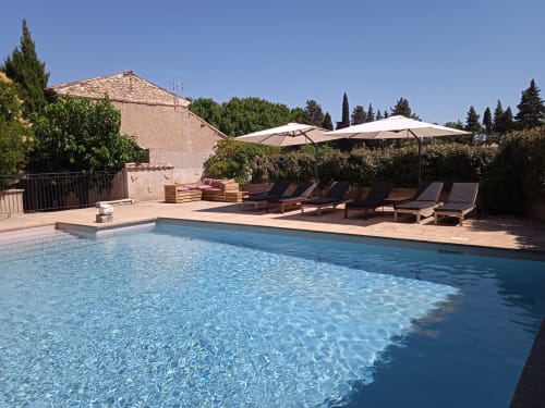 Crystal-clear pool at Mas des Artistes in Mouriès with lounge chairs and umbrellas, surrounded by trees and stonework