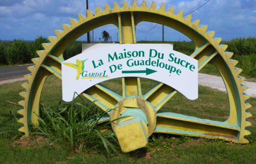 Gigantesque engrenage jaune de moulin à sucre avec pancarte Guadeloupe à la Résidence Les 2 Moulins au Moule