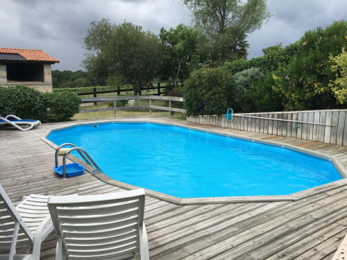 Piscine ovale bleu vif entourée d'une terrasse en bois au gîte Sous Les Marronniers à Petit Palais Cornemps, France