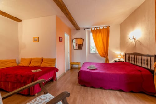 Chambre lumineuse et colorée à la maison d'hôtes Les2lions à Vernet-les-Bains avec lit rouge, accents orange, poutres en bois et vue montagne