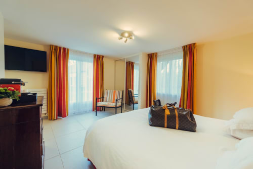 Spacious hotel bedroom at Clos Céleste in Ecrainville with white bed, red curtains, and flat-screen TV