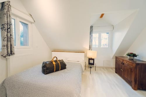 Bright attic bedroom at Clos Céleste with queen bed, wooden dresser, and windows overlooking the pool at this Etretat