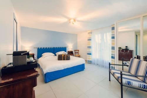 Spacious bedroom at Clos Céleste with blue bed, white linens, striped chairs, and modern amenities in Ecrainville