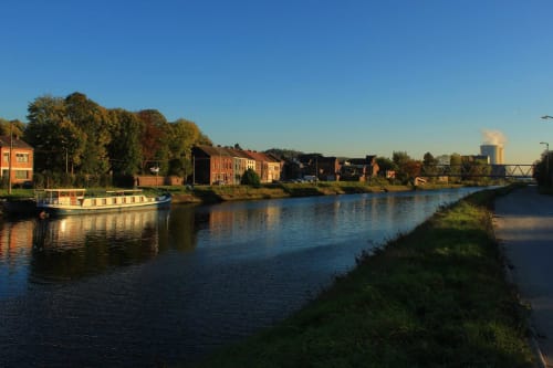 Vue fluviale de Marcinelle avec ses bâtiments en briques rouges traditionnels, bateau amarré et paysage industriel à la Résidence