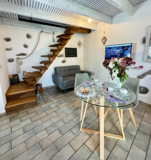 Séjour moderne avec escalier en bois, table à manger, fauteuil gris et fleurs à l'Agritusmo Stecadò