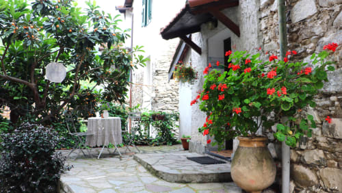 Charmante cour de jardin à l'Agritusmo Stecadò à Dolceacqua avec des géraniums rouges, des murs en pierre et des pots en terre cuite rustiques
