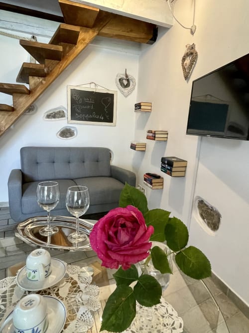 Séjour cosy du loft d'Agritusmo Stecadò avec canapé gris, rose rose, verres de vin, escalier bois et décoration murale