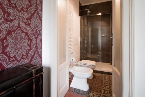 Bagno moderno a Porta Tosa Milano con sanitari bianchi, doccia scura, carta da parati damascata rossa e piastrelle geometriche