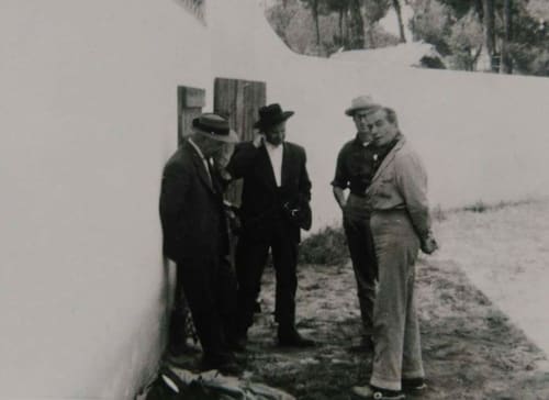 Quatro homens em roupas vintage conversando em frente ao Patio Da Villa, uma pensão com paredes brancas em Coruche, Portugal