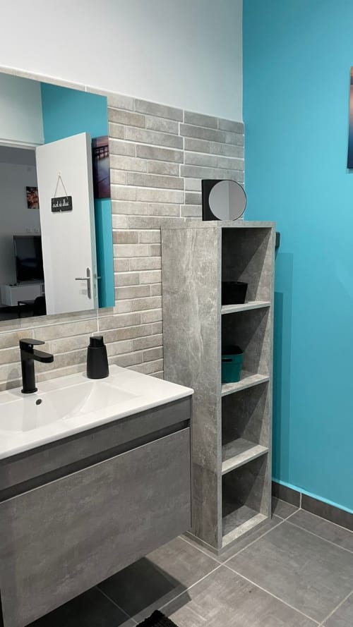 Salle de bain moderne à la villa Kaz A Bibi à Sainte-Rose avec murs turquoise, carrelage gris, lavabo blanc et accessoires noirs