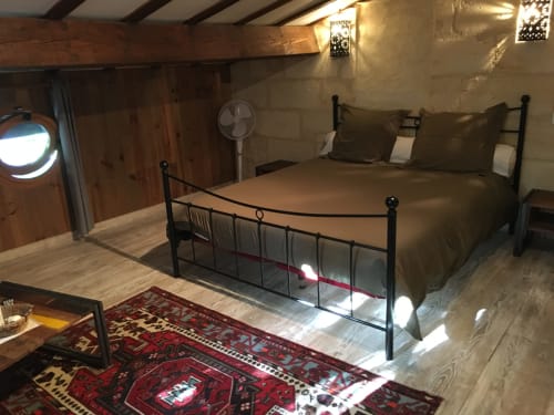 Chambre aux Marronniers avec lit en fer forgé, poutres apparentes, tapis persan rouge et vue sur le jardin