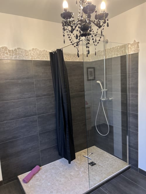 Luxuriöses Badezimmer im Gabrielle Chanel Zimmer des Château Ségot mit begehbarer Dusche, Kronleuchter und eleganten dunklen Fliesenoberflächen