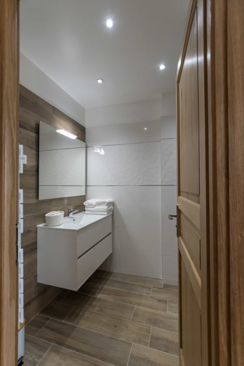 Salle de bain moderne à La Vallee Joly B&B au Vast avec vanité blanche, carrelage ton bois et douche