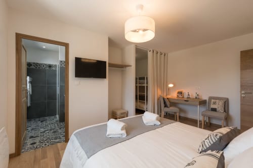 Chambre moderne à La Vallee Joly au Vast avec salle d'eau, TV écran plat, bureau et mobilier contemporain.