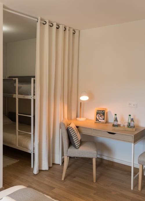 Chambre d'hôtel moderne à La Vallee Joly avec rideaux crème, bureau avec lampe, chaise et lit mezzanine à Le Vast, France