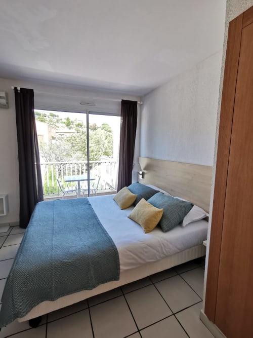 Chambre lumineuse à la Résidence Saint Michel avec lit queen-size, balcon vue sur L'île Rousse et équipements modernes incluant climatisation