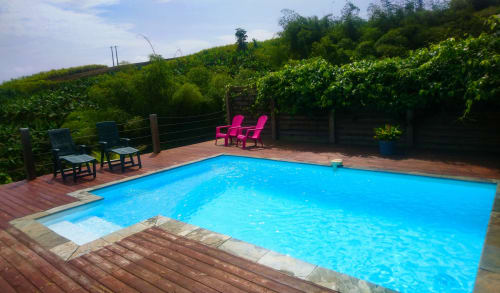Piscine aux eaux bleu vif, terrasse en bois, chaises Adirondack roses et verdure luxuriante à Villa Tourmaline