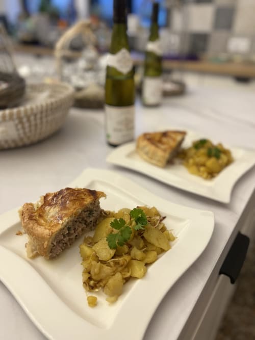 Plat de viande accompagné de pommes de terre rôties et d'herbes au Château Ségot, Neuilly-le-Réal, bouteilles de vin en arrière-plan