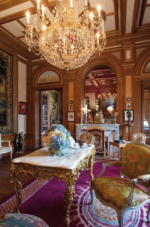 Élégant salon français du Château Ségot avec lustre en cristal, boiseries ornées, table en marbre et mobilier d'époque.