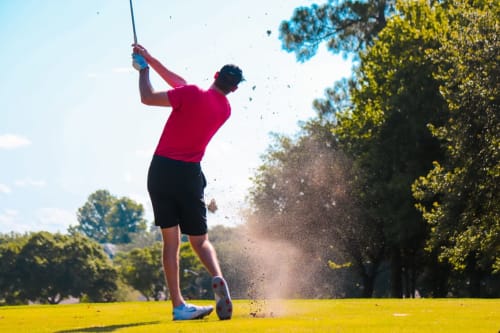 Golfeur en swing au Château Ségot à Neuilly-le-Réal, France, avec parcours verdoyant et arbres