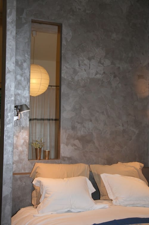 Chambre Airbnb à Marseille aux murs gris texturés, literie blanche, lampe suspendue en papier luminescente, et niches modernes