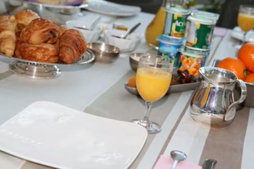 Table du petit-déjeuner à la Campagne d'Albert B&B à Marseille avec croissants, jus d'orange, fruits frais et couverts