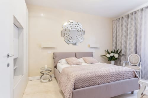 Camera moderna alle Petra Apartments Rome con letto tortora, specchio rotondo, comodini bianchi e tende con vista sulla città