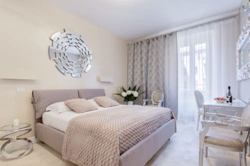 Camera elegante e spaziosa di Petra Apartments Roma con letto grigio, specchio decorativo e vista sulla città attraverso tende trasparenti