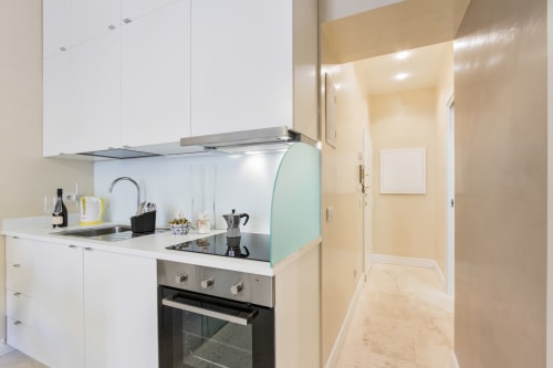 Cucina moderna negli Appartamenti Petra Roma con mobili bianchi, elettrodomestici in acciaio inossidabile e schienale verde menta
