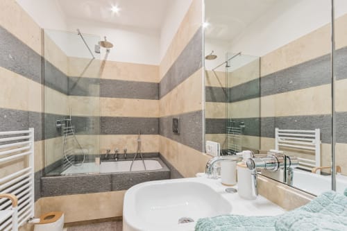 Bagno moderno a Petra Apartments Roma con piastrelle righe, doppio lavabo, vasca, doccia pioggia e scaldaracchino