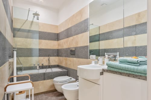Bagno moderno presso Petra Apartments Roma con piastrelle a righe, vasca da bagno, doccia, WC, lavandino e asciugamani verdi